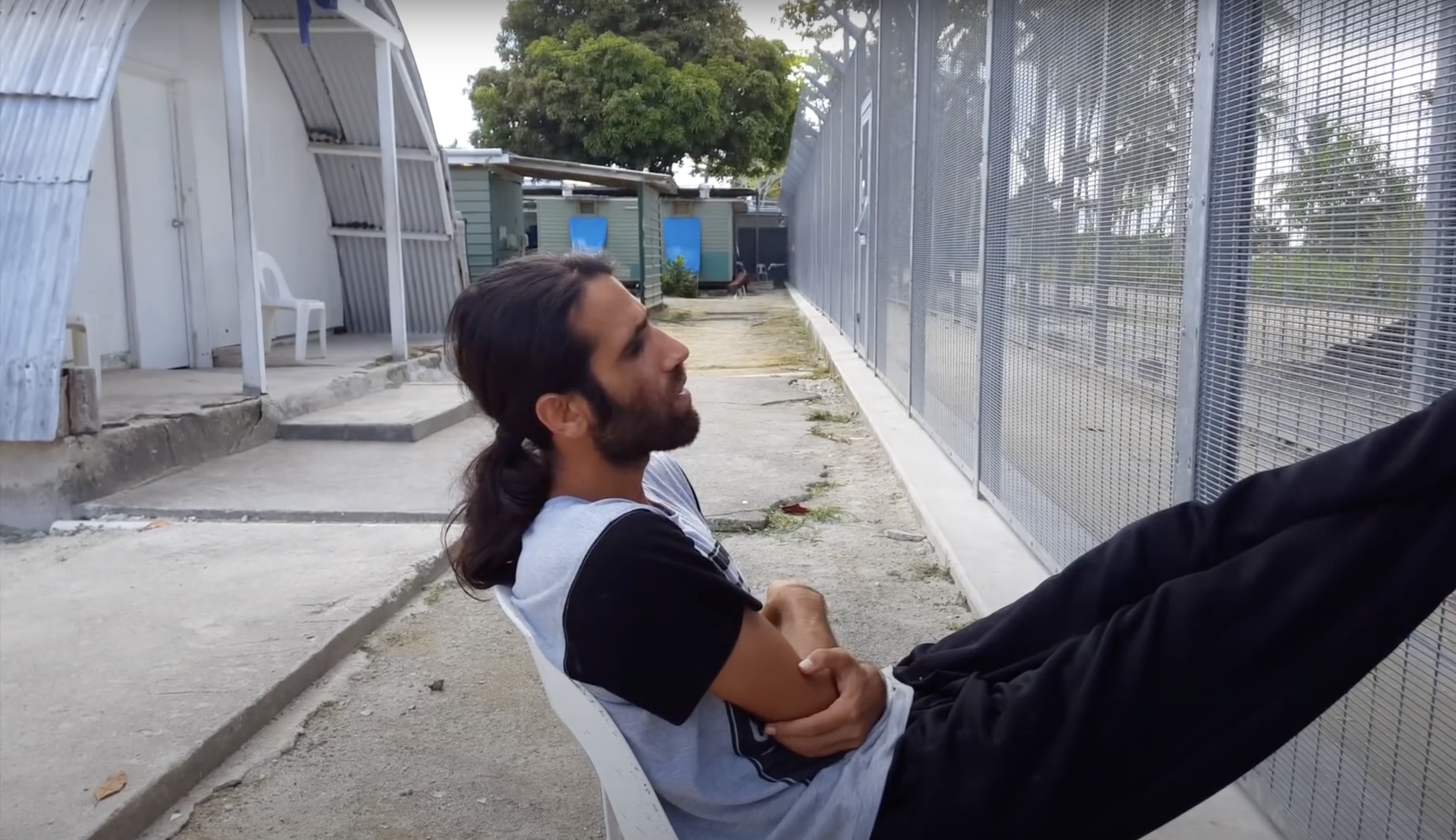 <p>Arash Kamali Sarvestani and Behrouz Boochani, <em>Chauka, Please Tell Us The Time</em> (2017), video still, depicting Behrouz Boochani by the fence at Manus Regional Processing Centre, before its closure and detainees were moved to other facilities on the island.</p>